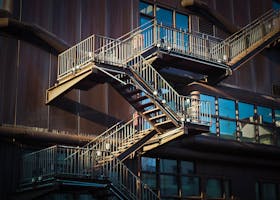 Home Steel staircase with rusty facade and glass windows on an urban building in daylight.
